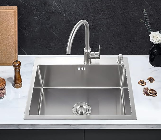 Fregadero de cocina de acero inoxidable con grifo, tabla de cortar y accesorios sobre encimera.