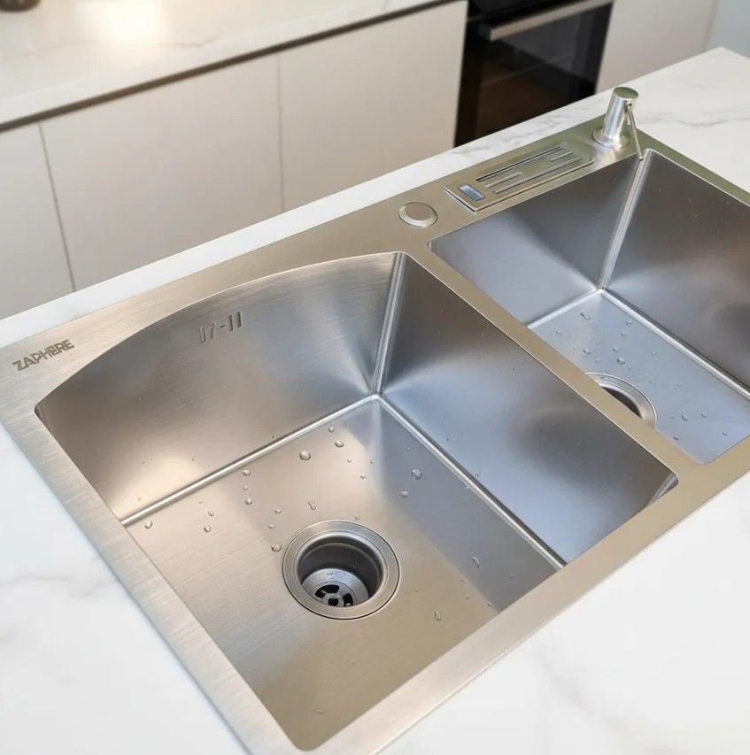 Fregadero de cocina de acero inoxidable con grifo y dispensador de jabón sobre encimera oscura.