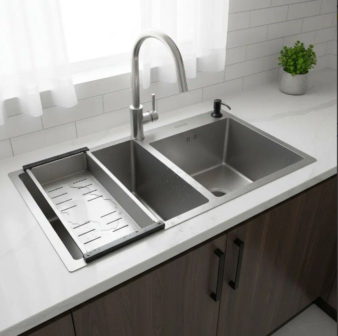 Fregadero de cocina de acero inoxidable con escurridor, grifo y dispensador de jabón integrados. Instalado sobre una encimera blanca.