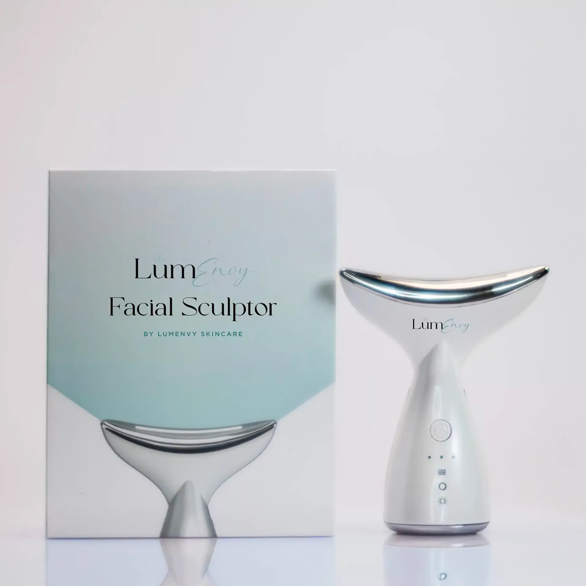 Facial sculpting device and box. Device is white and silver, box is white with text and a teal-colored graphic.