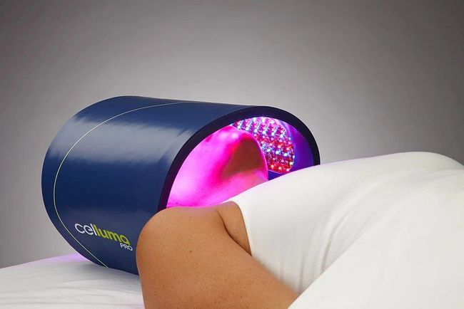 Person receiving light therapy under a blue cylindrical device emitting purple light.
