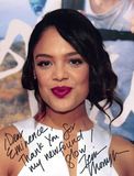 Tessa Thompson with dark hair, a deep pink lipstick, smiles, and a handwritten autograph.