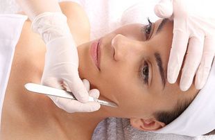 Person receiving facial dermaplaning. Gloved hands holding scalpel near face.