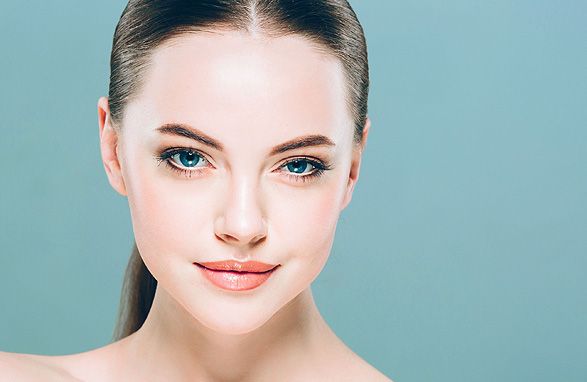 Woman with fair skin and blue eyes, looking towards the viewer, with a neutral expression. Light teal background.