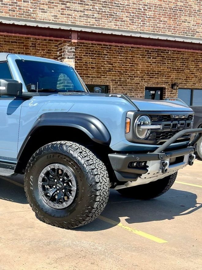 A blue ford bronco raptor is parked in a parking lot in front of a brick building.