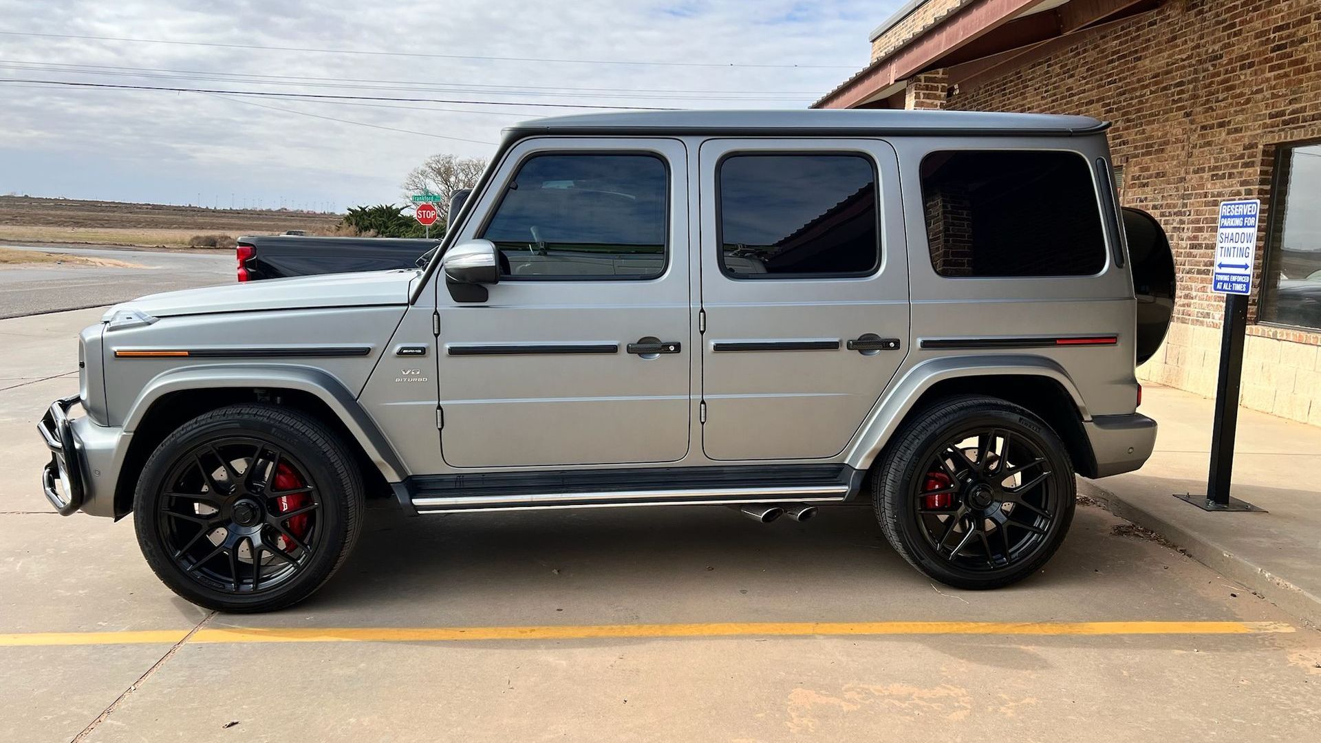 A silver mercedes benz g63 is parked in a parking lot.