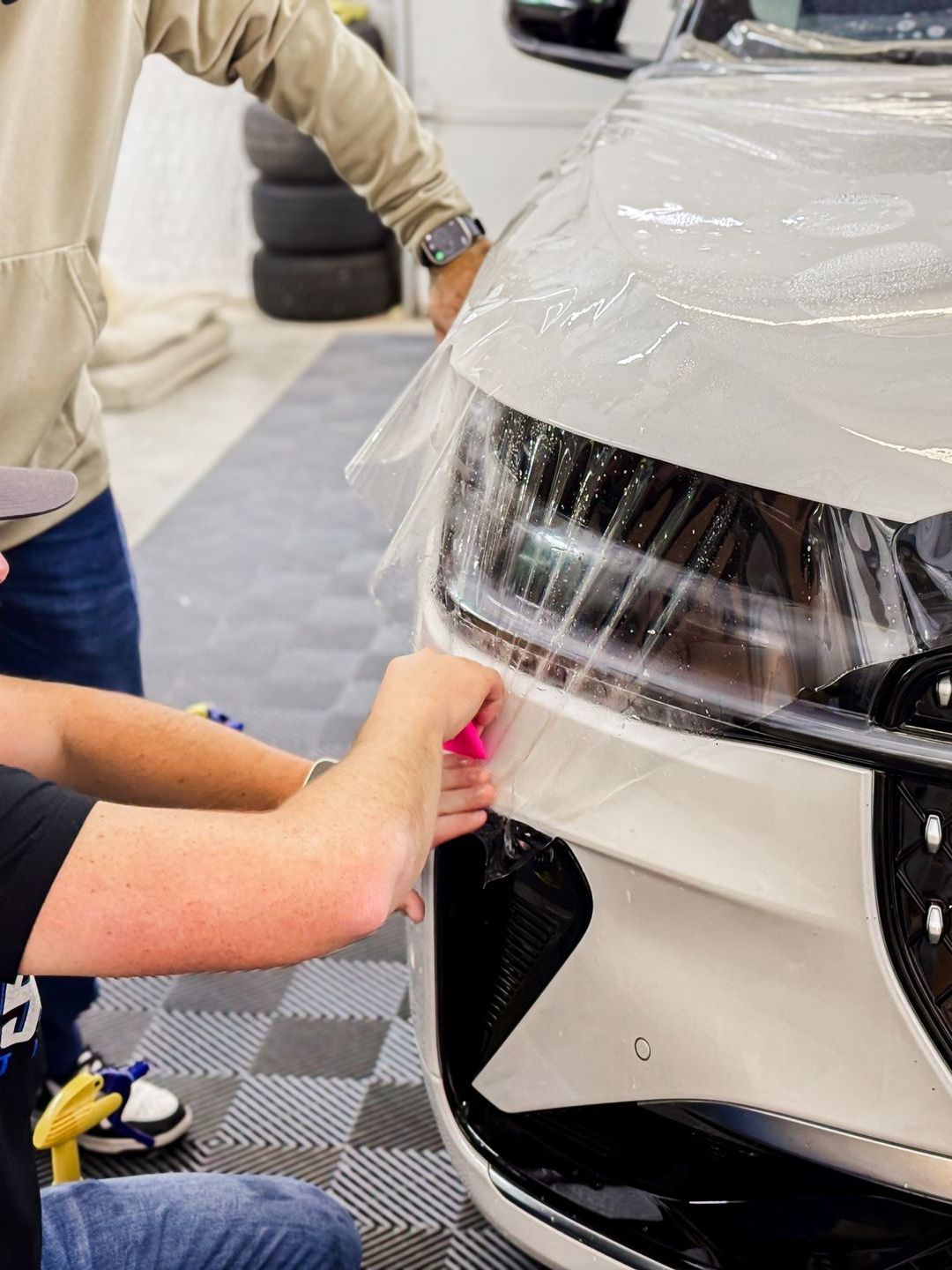 A man is applying a protective film to the front of a white car.