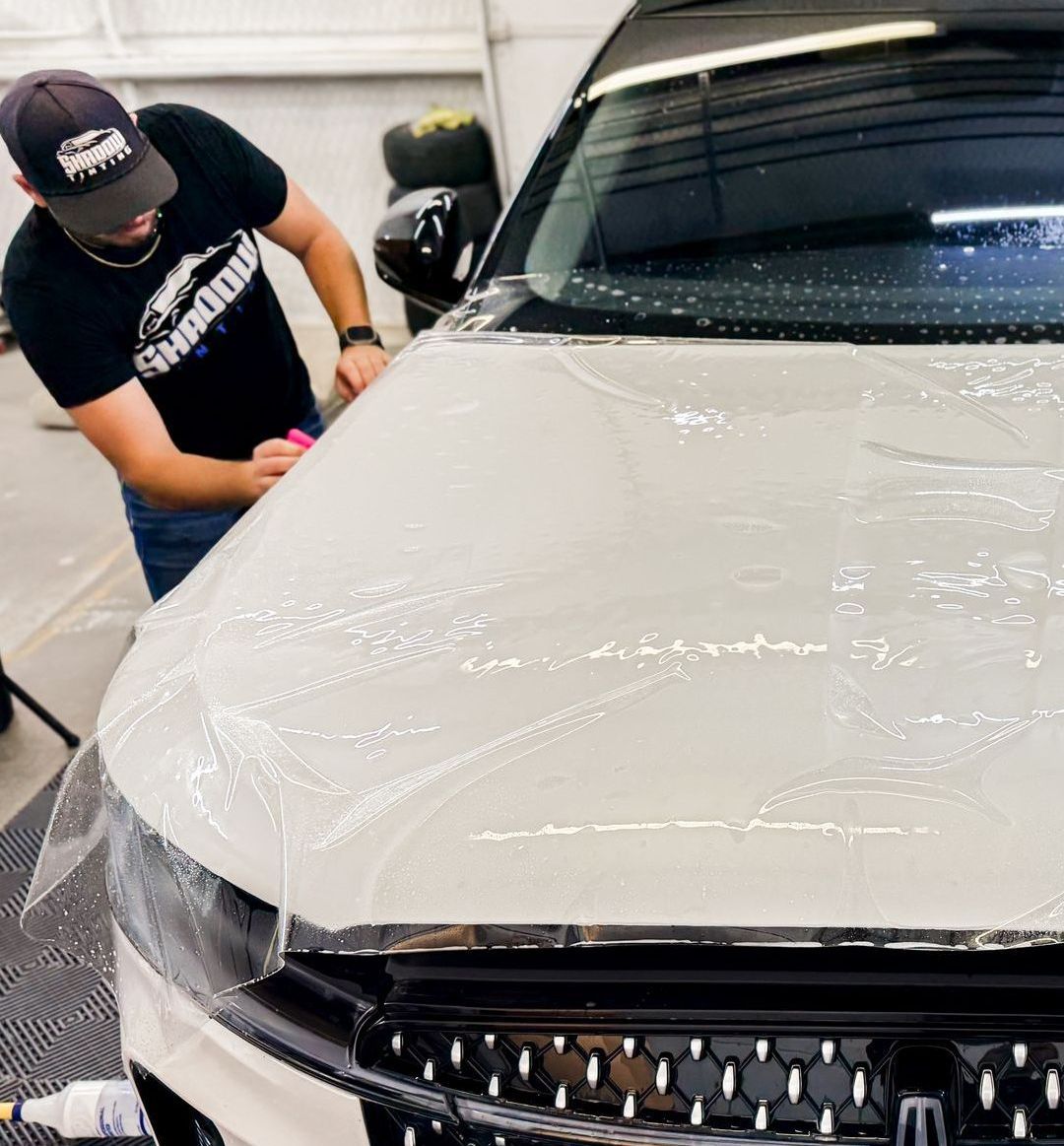 A man is covering the hood of a car with plastic wrap.