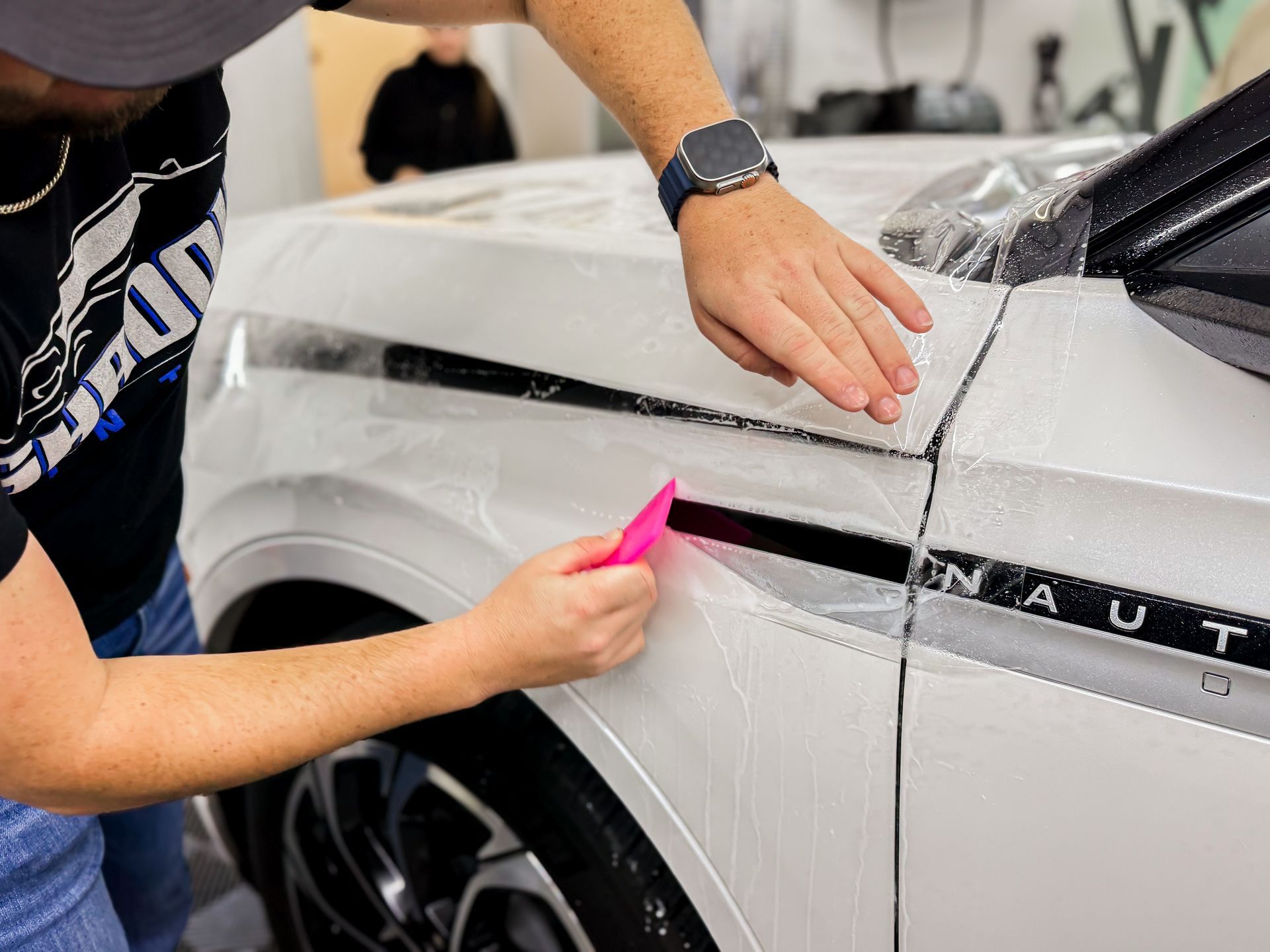 A man is applying a protective film to the side of a white car.
