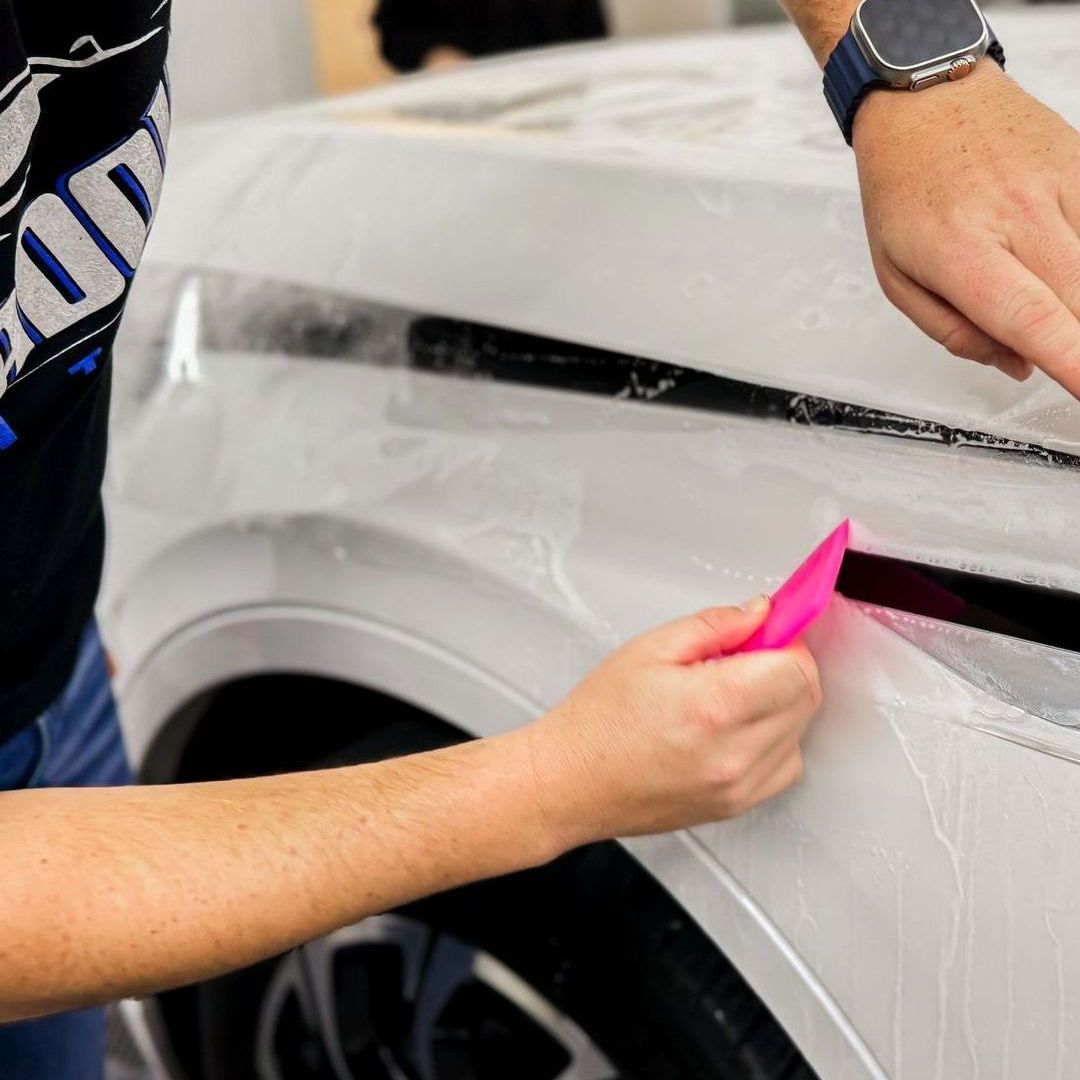 A person is applying protective film to a white car