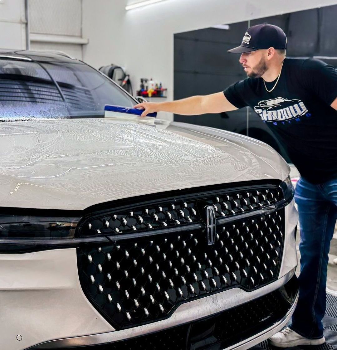 A man is cleaning the hood of a car in a garage.