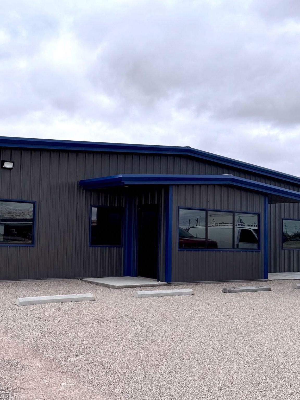 A large building with a blue roof is sitting on top of a gravel lot.