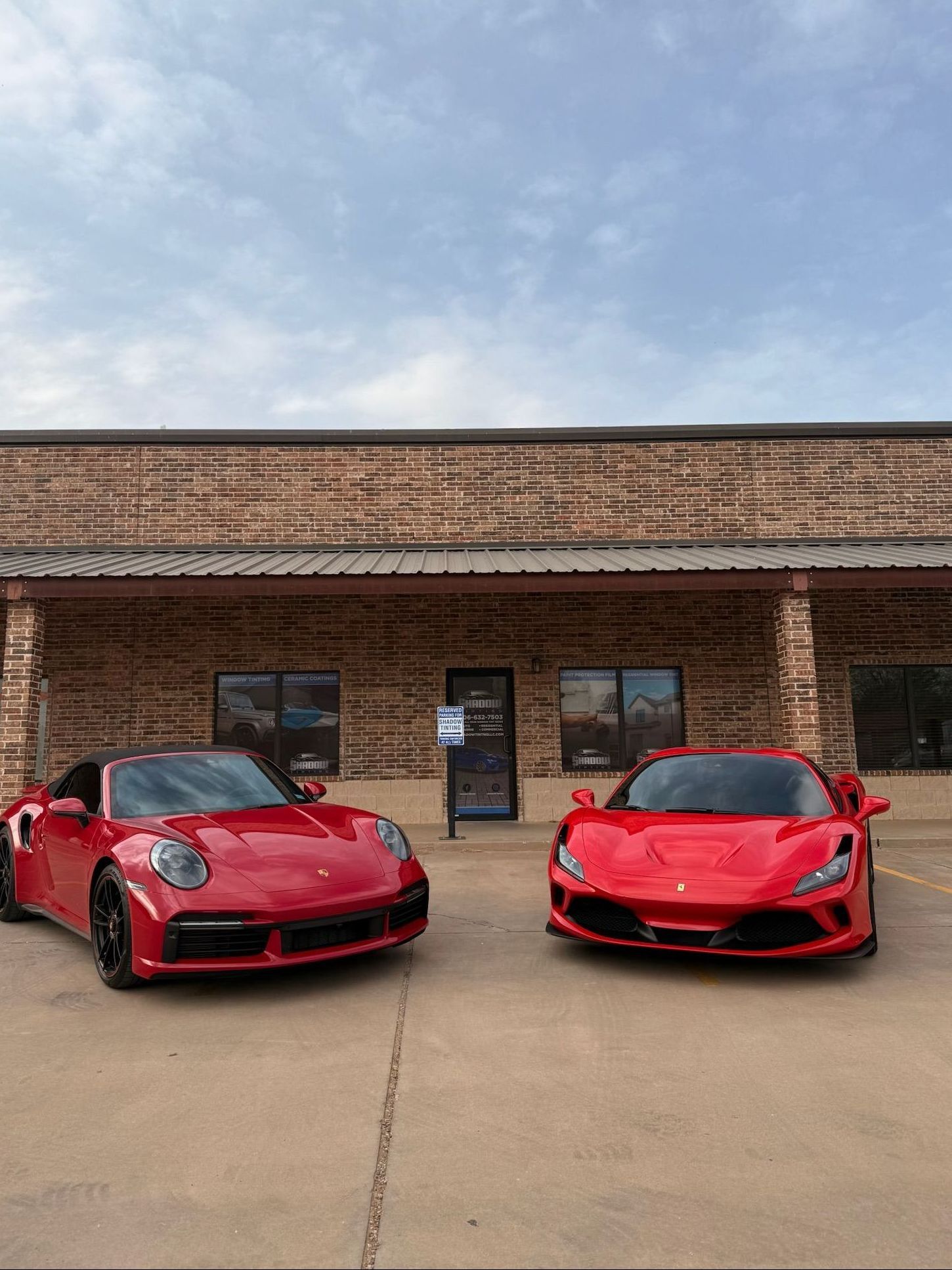 Two red sports cars are parked in front of a building.