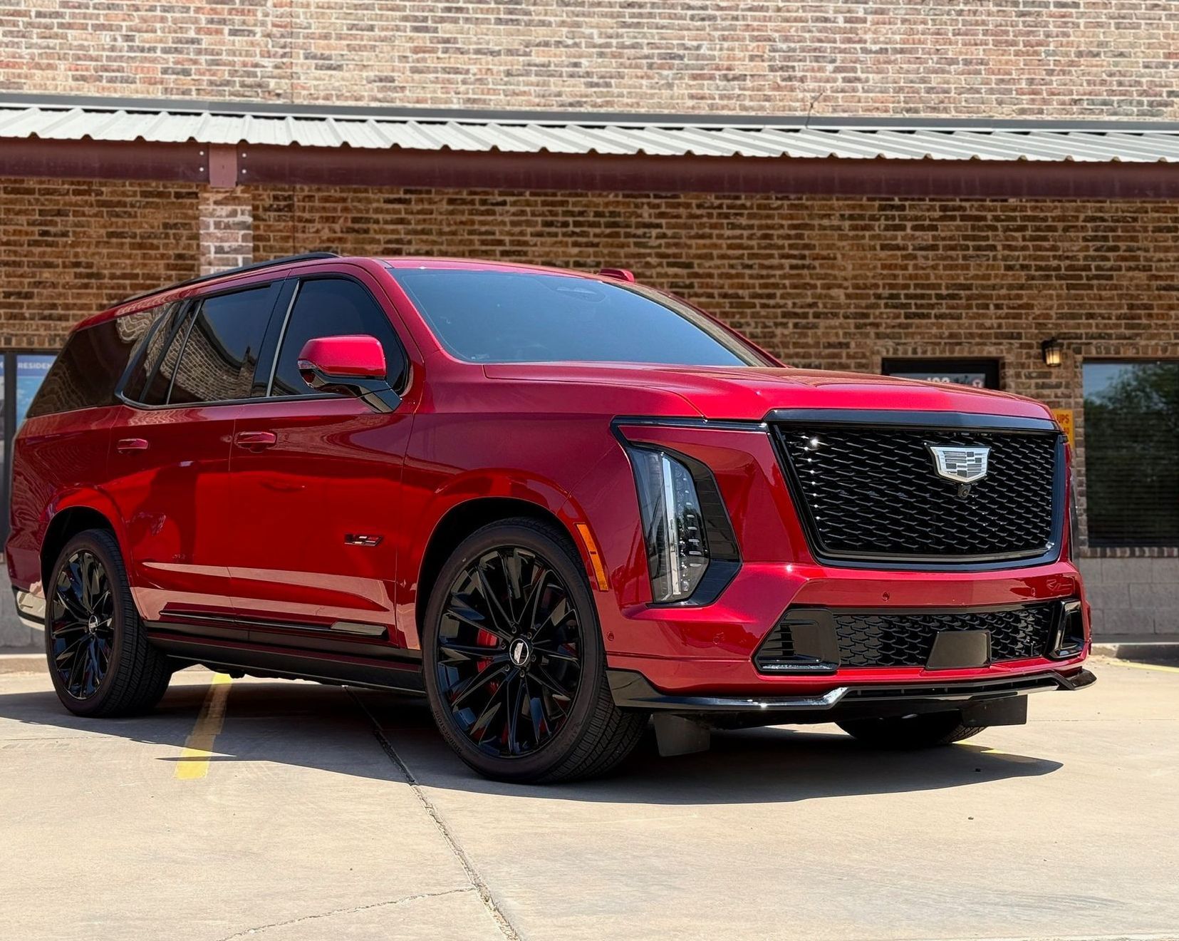 A red cadillac escalade is parked in front of a brick building.