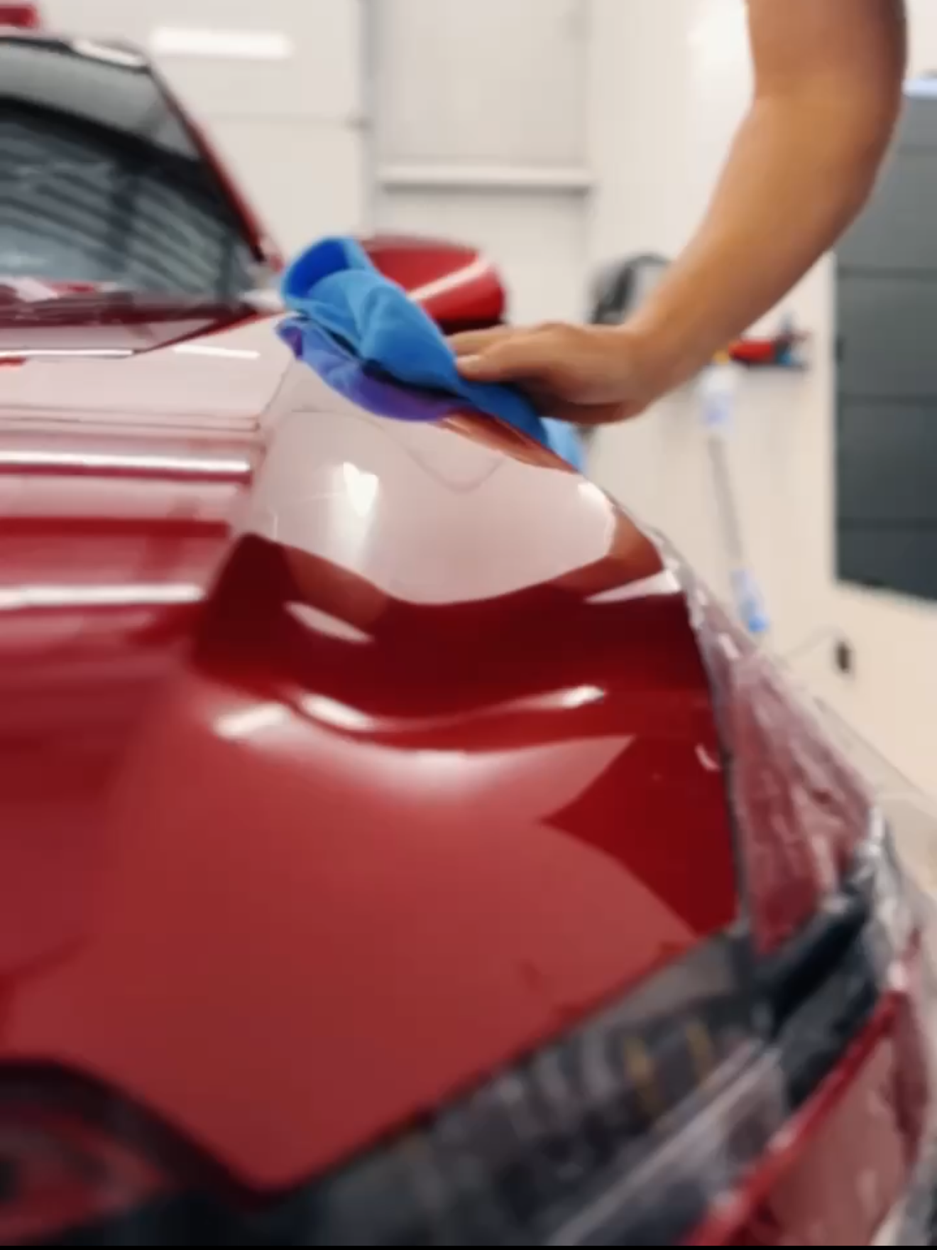 A person is cleaning a blue car with an orange towel