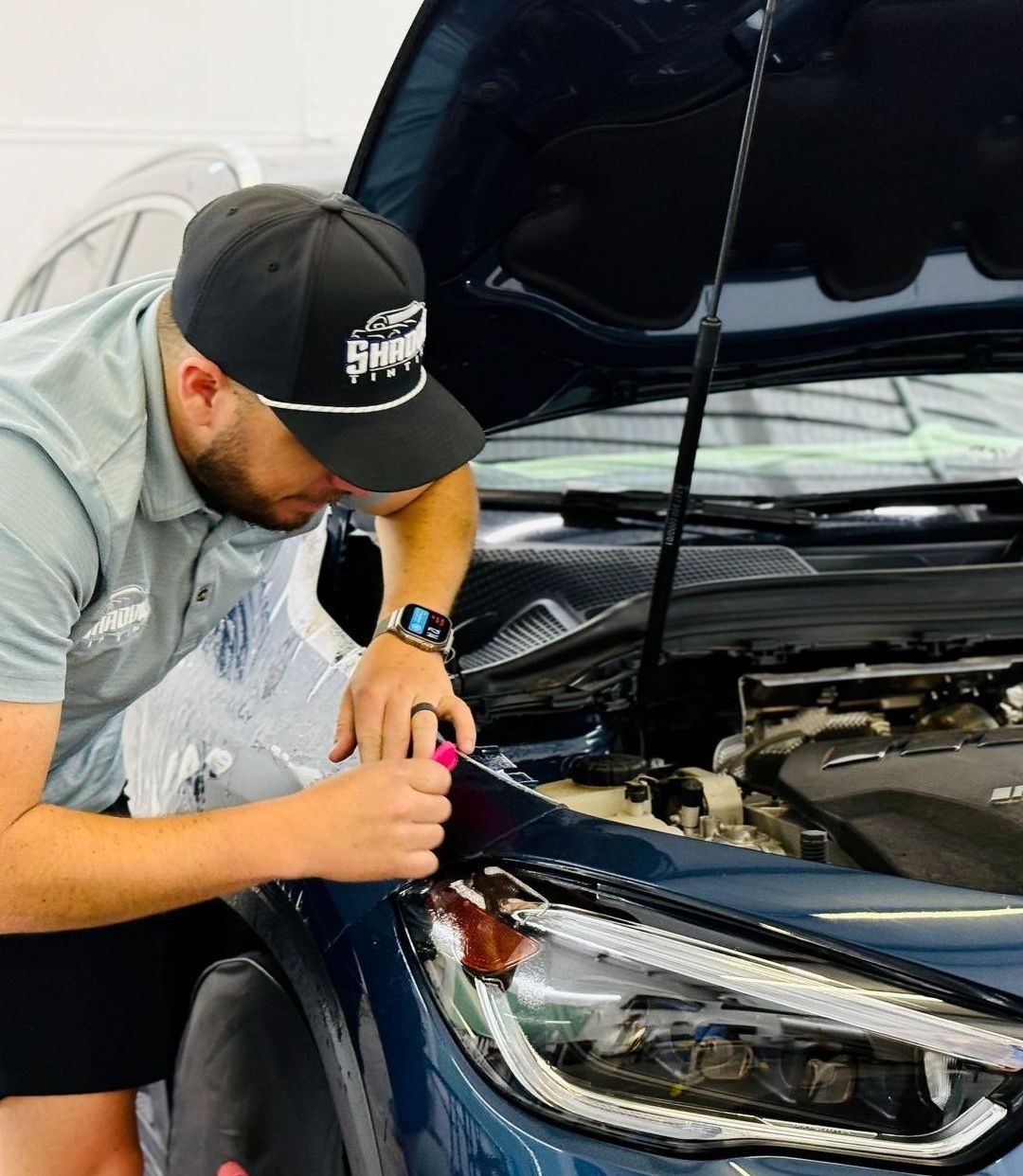 A man wearing a hat is working on a car with the hood open.