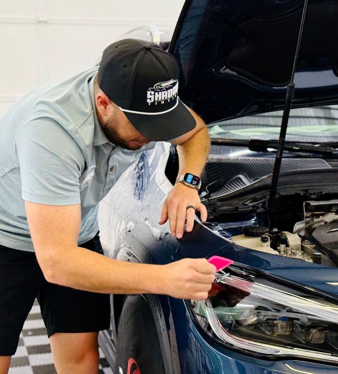 A man in a hat is working on a car with the hood open.