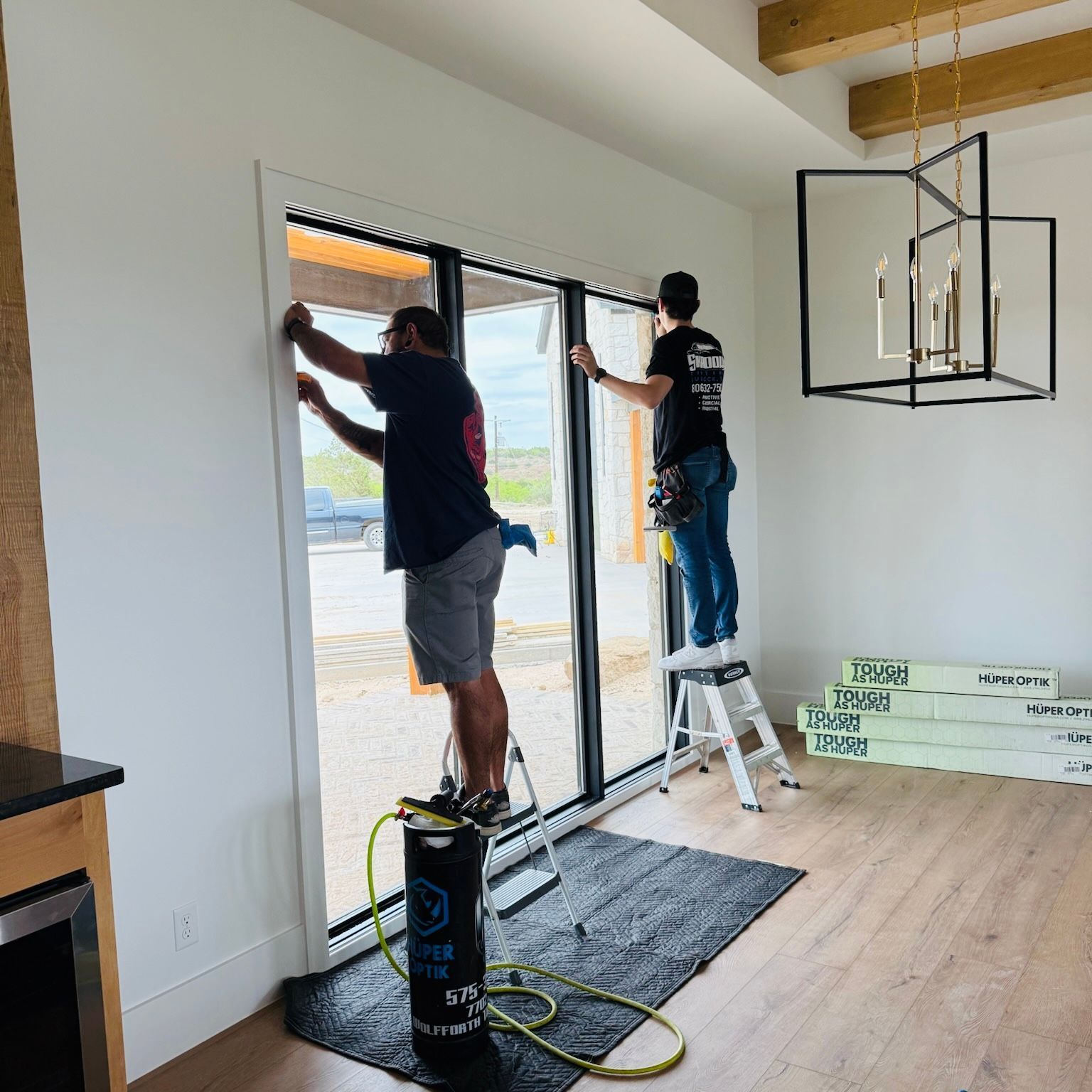 Two men are working on a window in a living room.