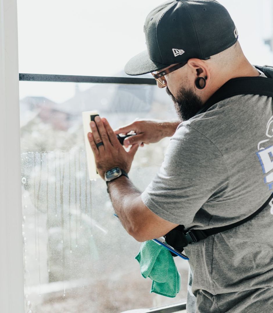 A man wearing a hat and sunglasses is cleaning a window.