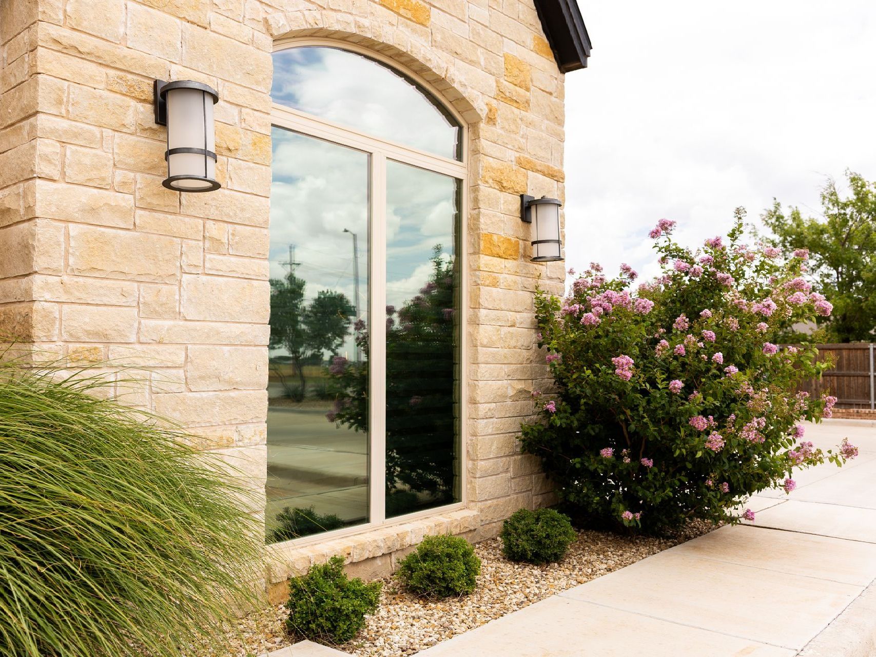 A brick building with a large window and a bush in front of it.