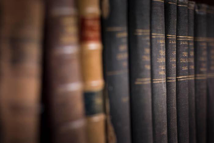 Close-up of worn leather-bound books on a bookshelf, with dark spines and gold lettering