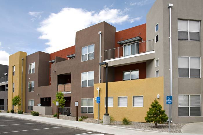 Modern apartment building with tan, brown, and gray facades along a street, with balconies and windows.