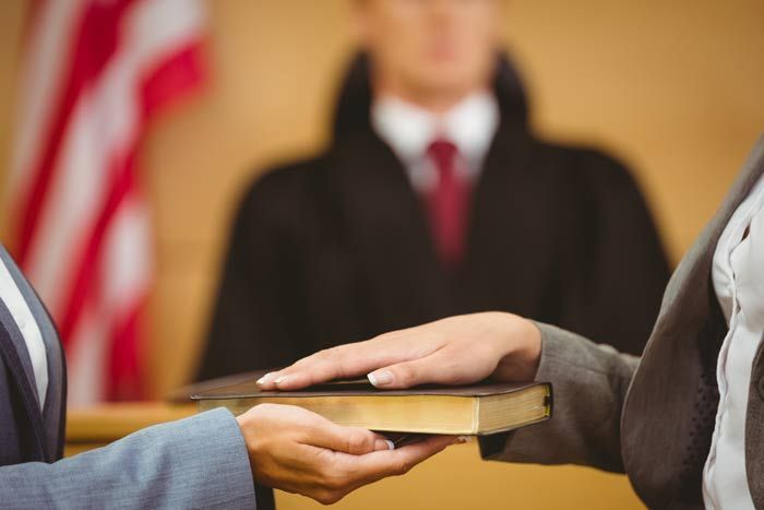 Hands passing a Bible in a courtroom with a judge blurred in the background