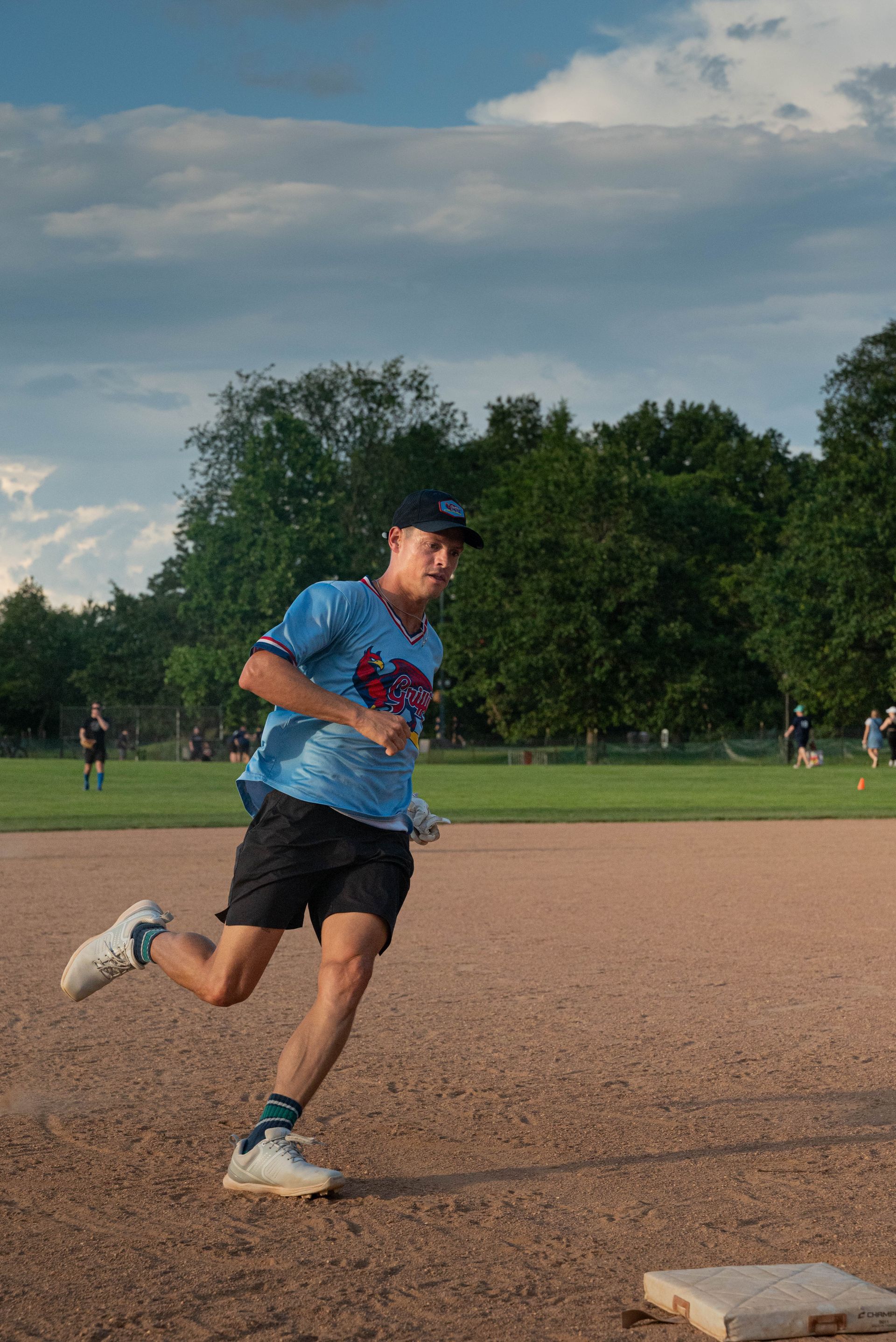A person wearing a hat and orange shirt, holding a baseball bat on their shoulder on a baseball field.