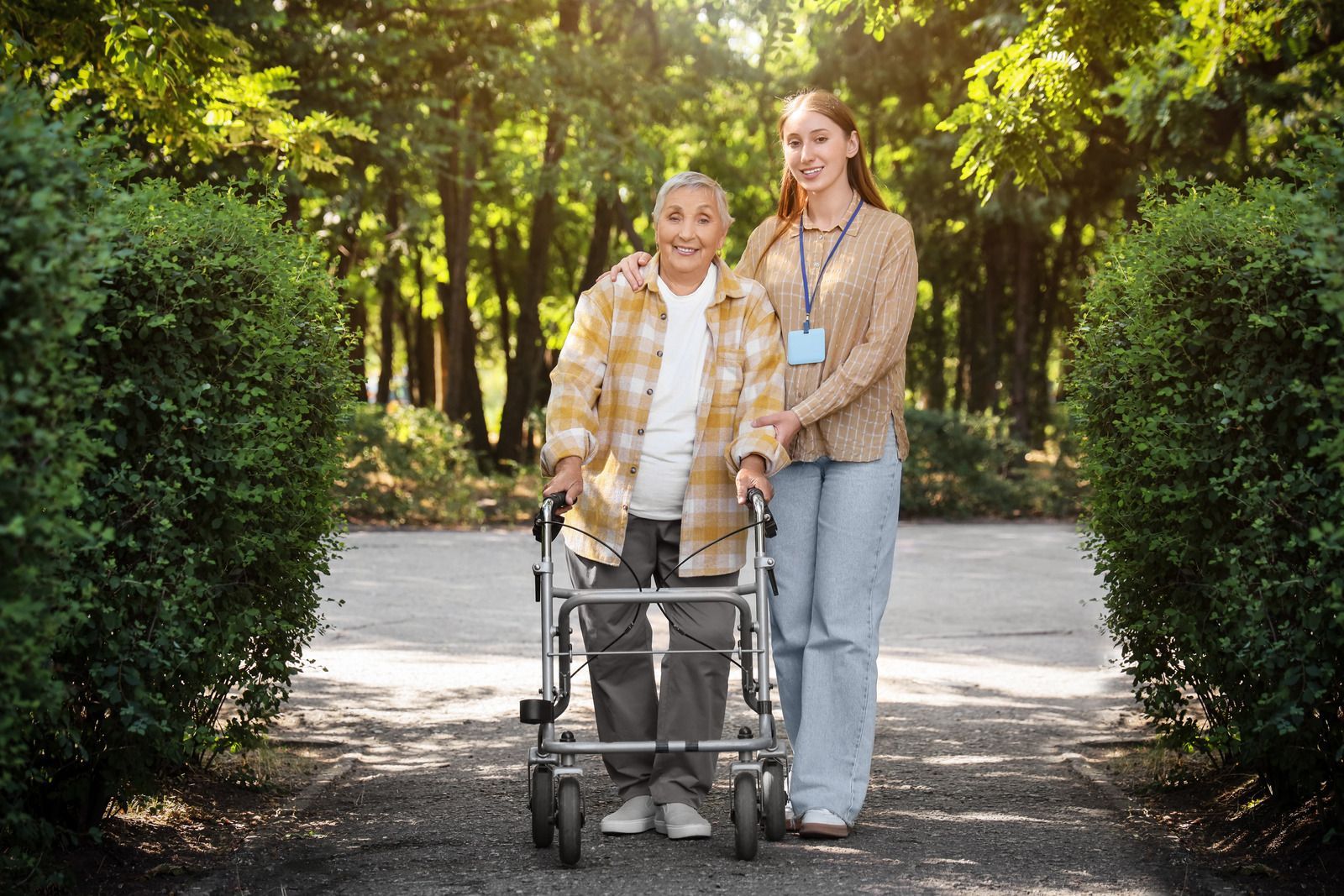 Woman with walker and caregiver walking in park.