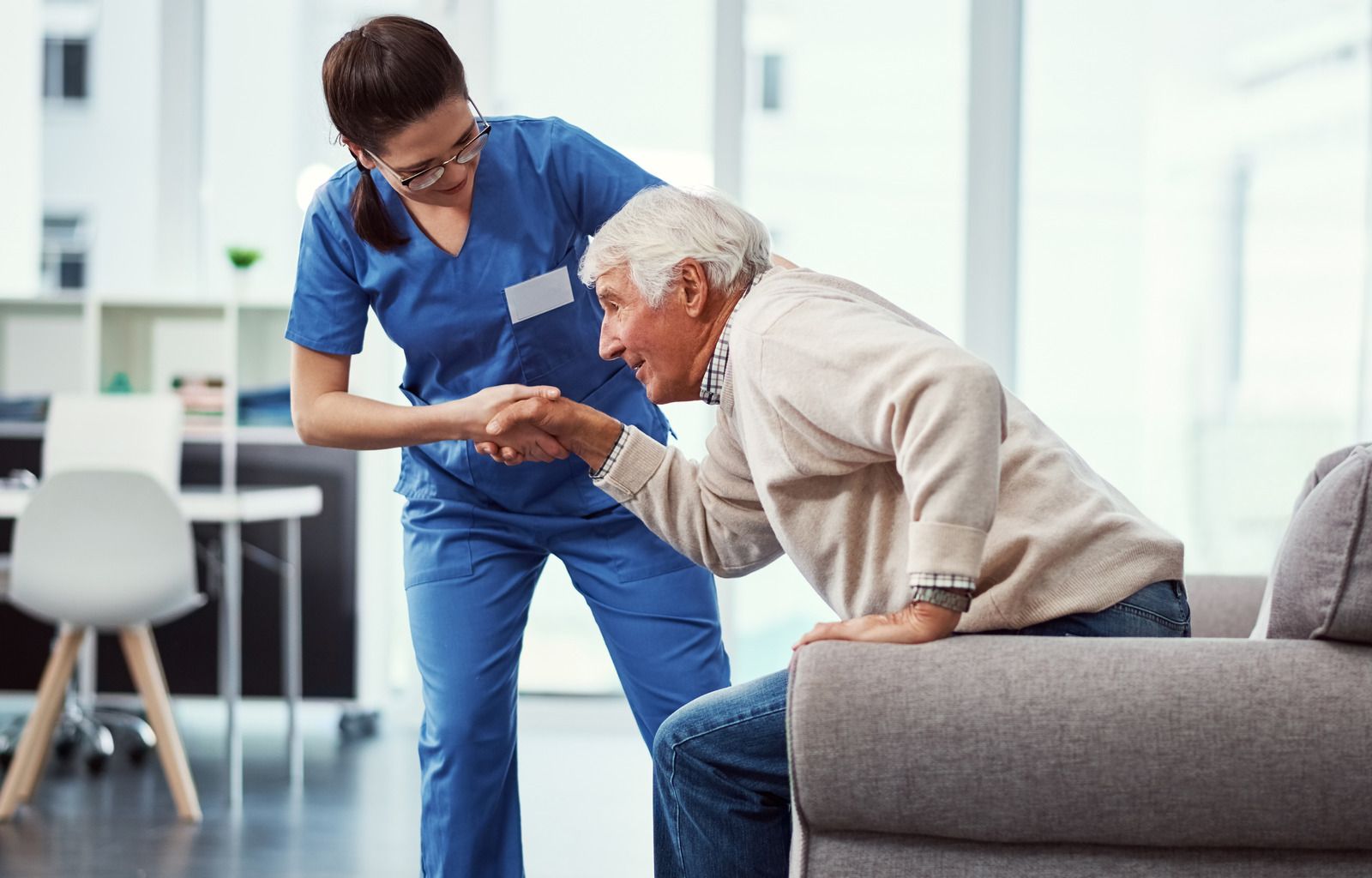 Medical staff, in scrubs, and other attire, join hands, smiling, in a healthcare setting.