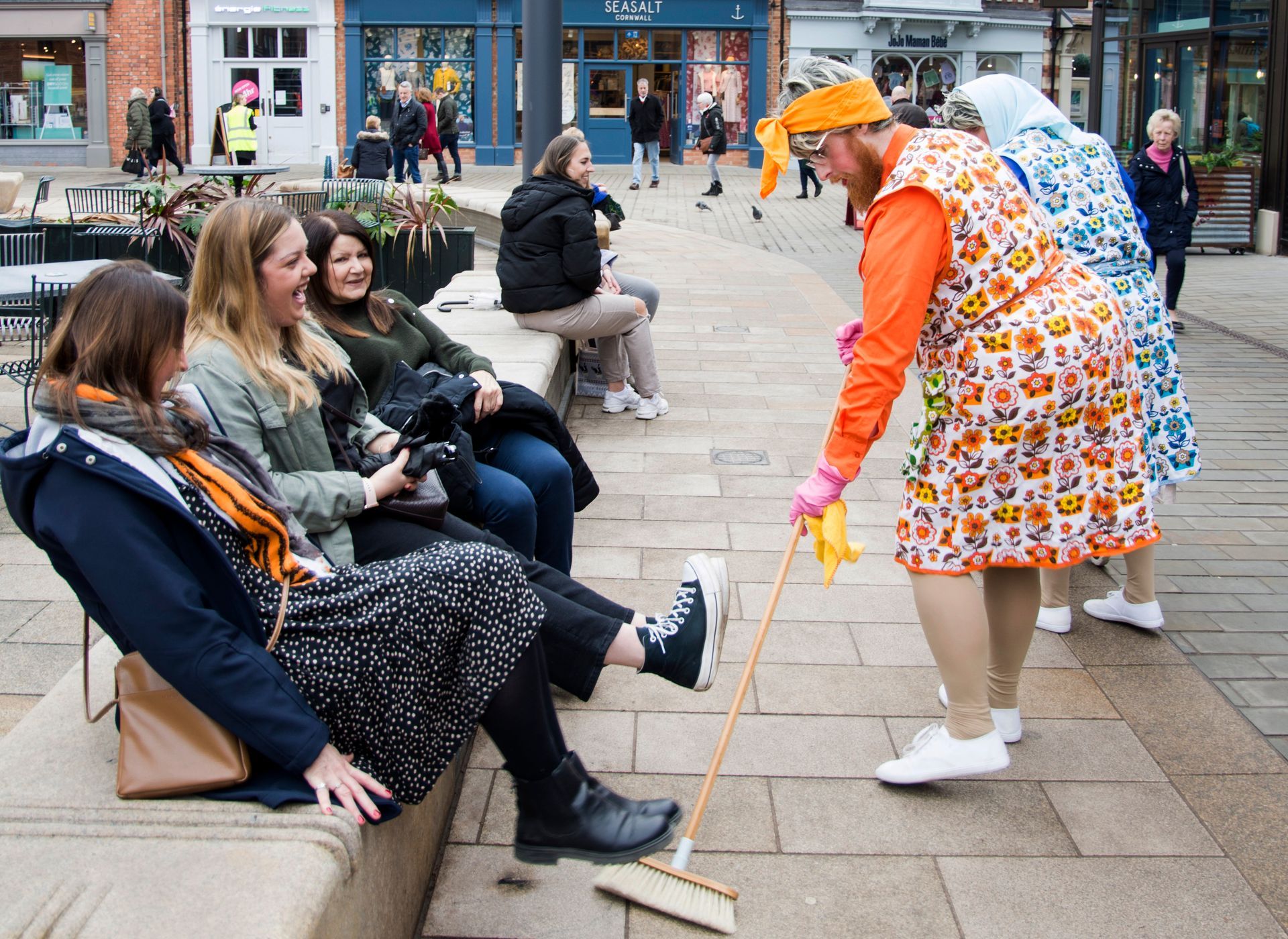 Dustbuster, Mildred, gets three members of public sat on a bench to raise their feet as she sweeps.