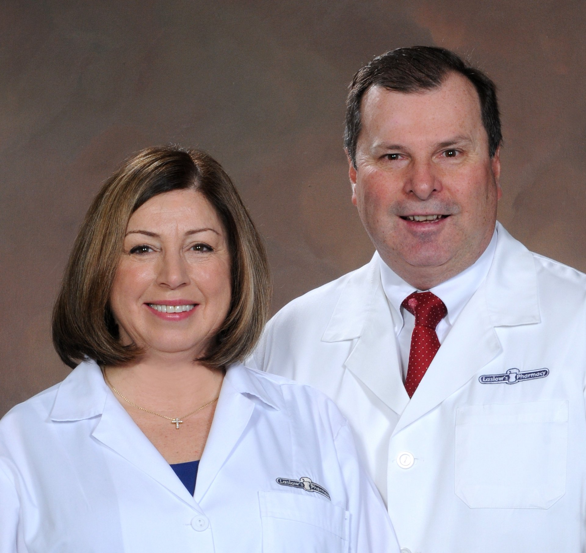 Two healthcare professionals in white coats smiling against a plain brown backdrop