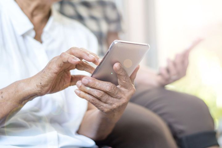 An elderly woman is using a smart phone while sitting on a couch.