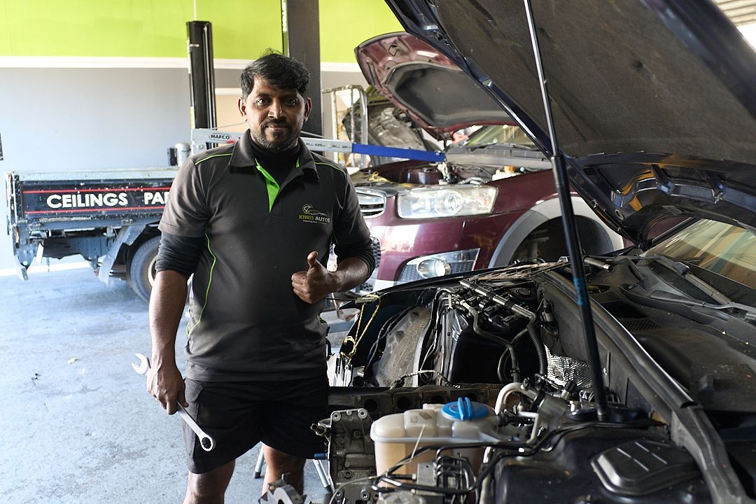 A man is standing in front of a car with the hood open.