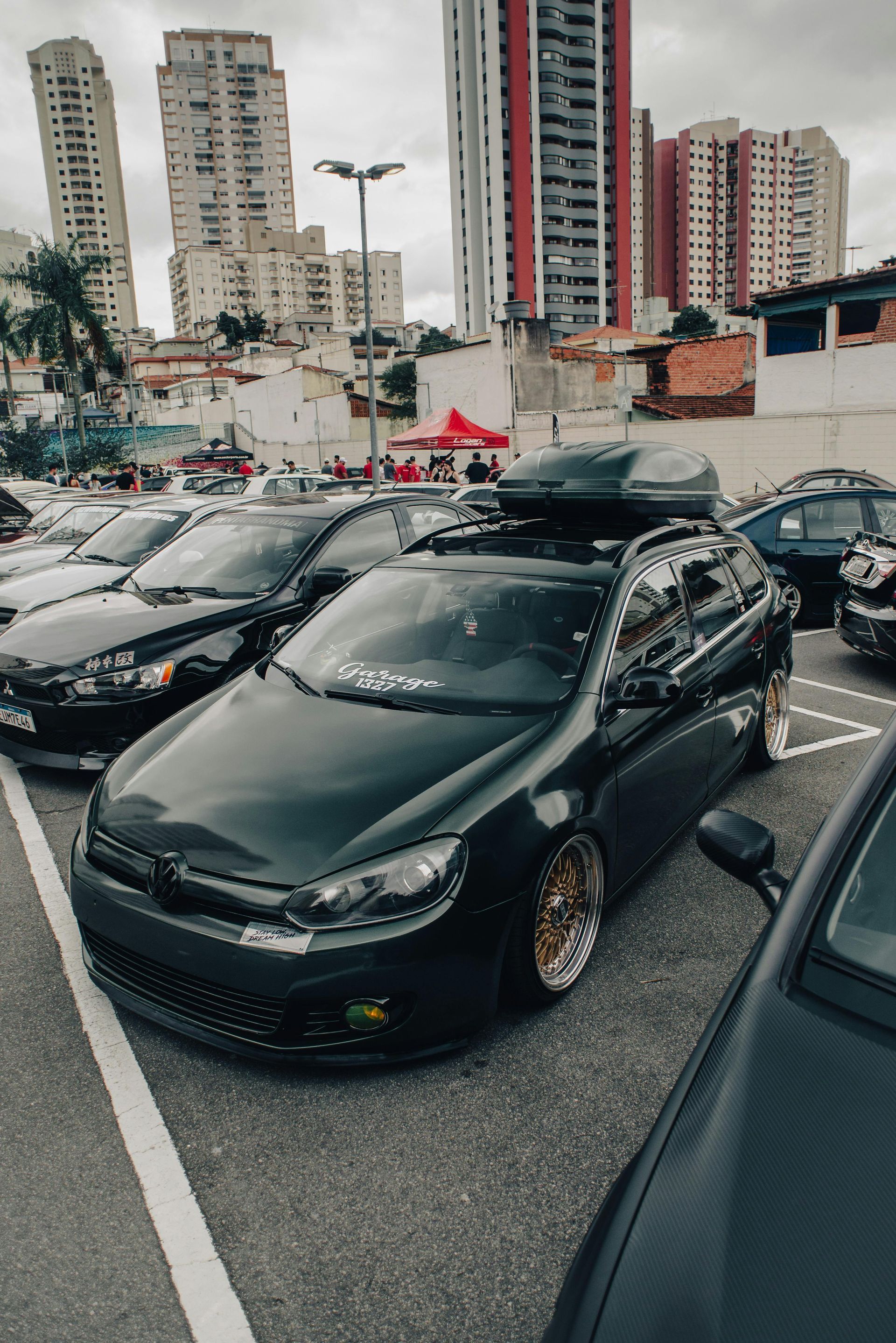 A black car with a roof box on top of it is parked in a parking lot.