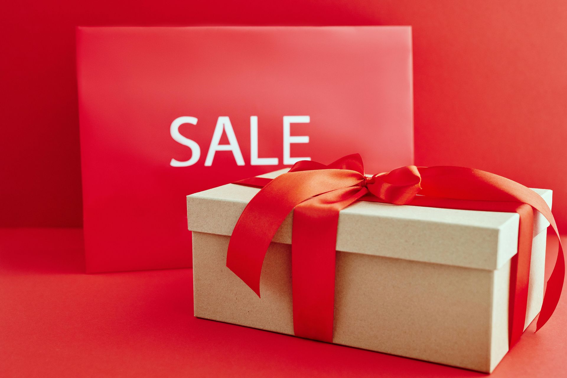 A white gift box with a red ribbon and bow on a red background.