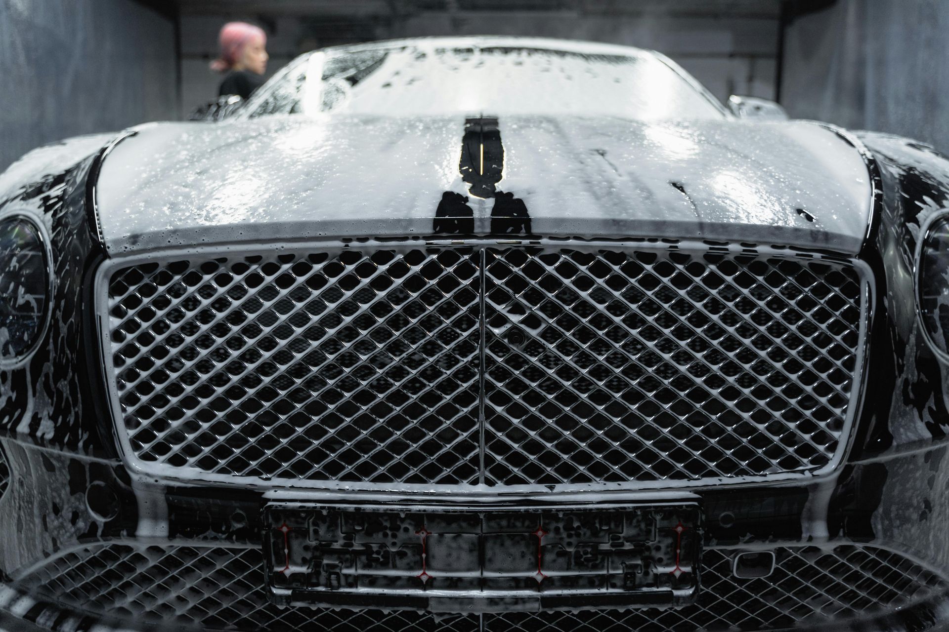 A black car is being washed with soap and water in a garage.