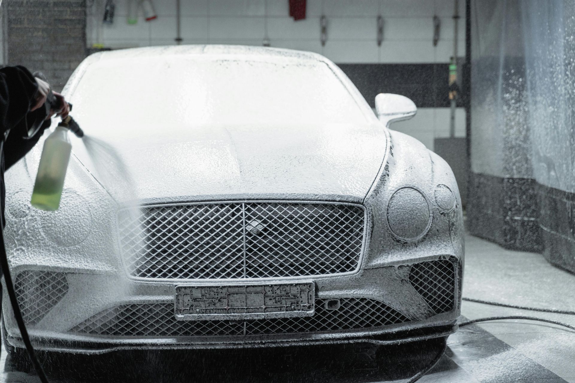 A bentley is being washed with foam in a garage.