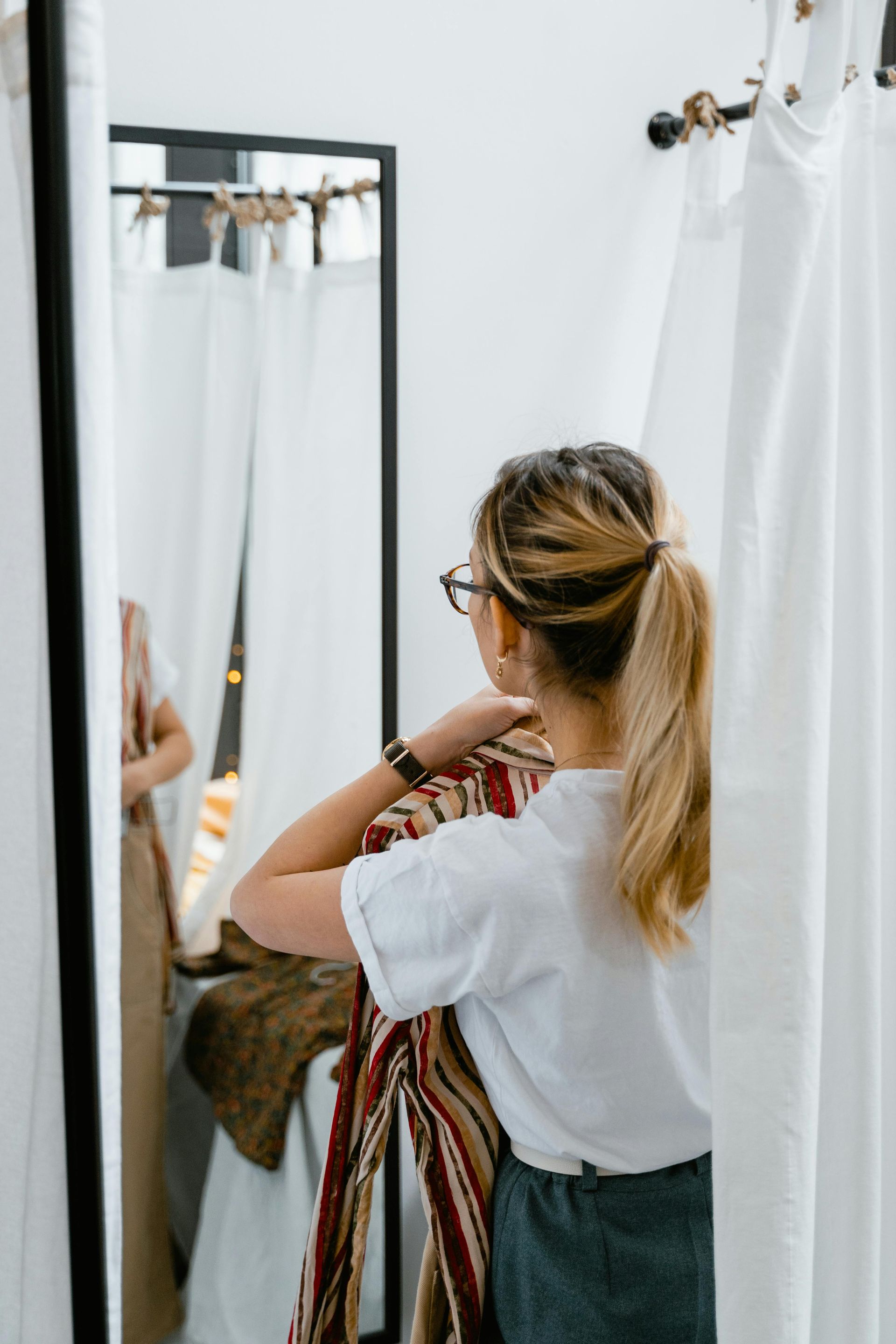 A woman is trying on a dress in a dressing room in front of a mirror.