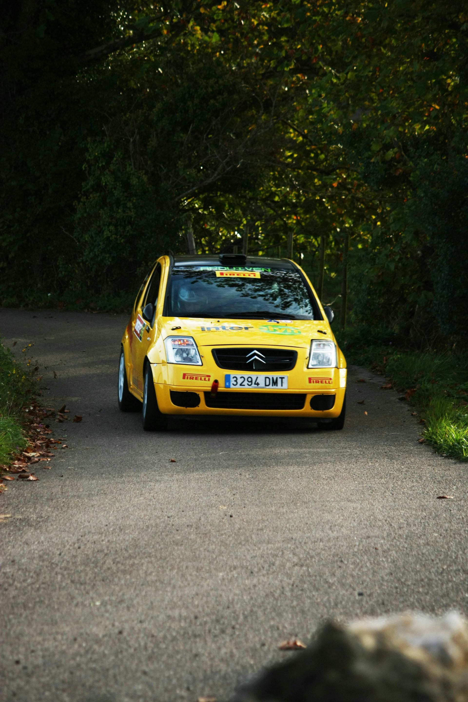 A yellow car is driving down a road in the woods.