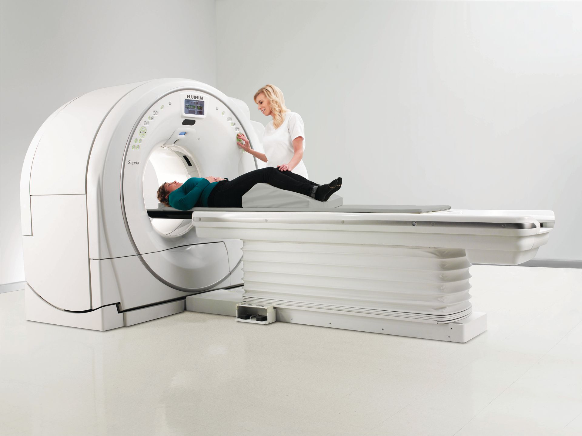 A woman is laying in a ct scan machine while a nurse looks on.