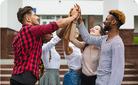 Group of diverse friends high-fiving, smiling joyfully outdoors in front of a building.