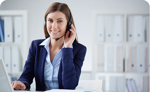 Woman in a business suit wearing a headset, smiling at a desk.