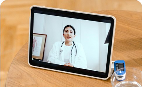 A tablet displays a female doctor conducting a telemedicine consultation; a pulse oximeter sits nearby.