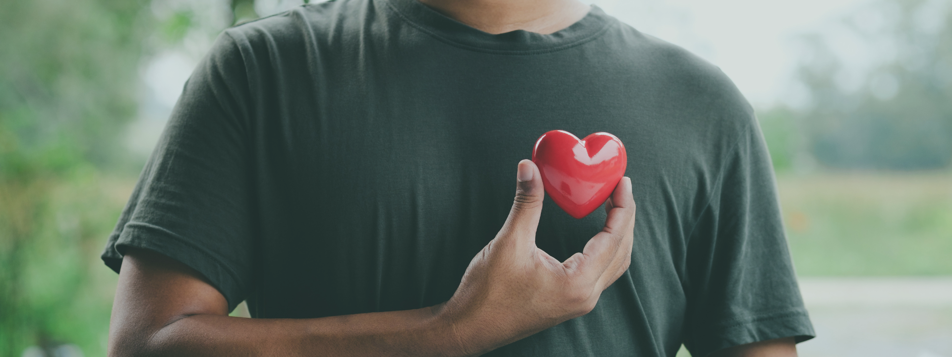 A person holding a red heart-shaped object against their chest. They wear a green t-shirt.
