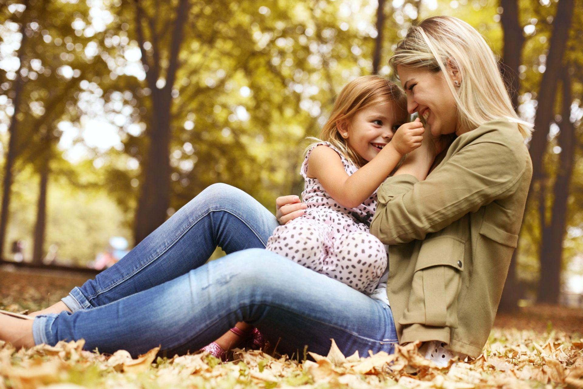Woman and young girl in a park, laughing while embracing each other amongst fall leaves.