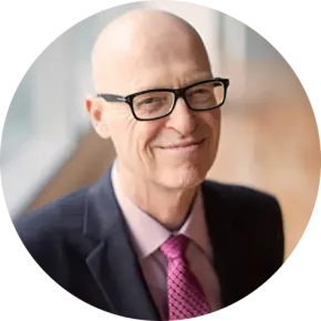 Bald man with glasses in suit and tie smiles.