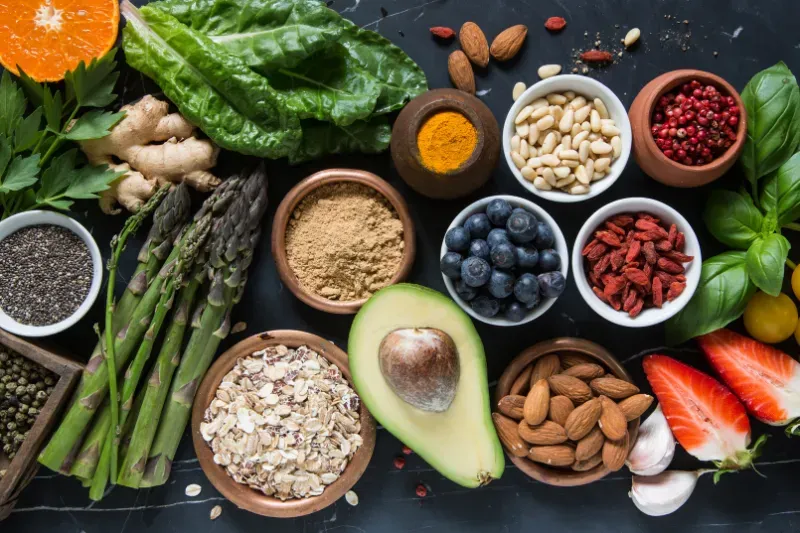 Overhead shot of various healthy foods in bowls, including fruits, vegetables, nuts, and seeds.