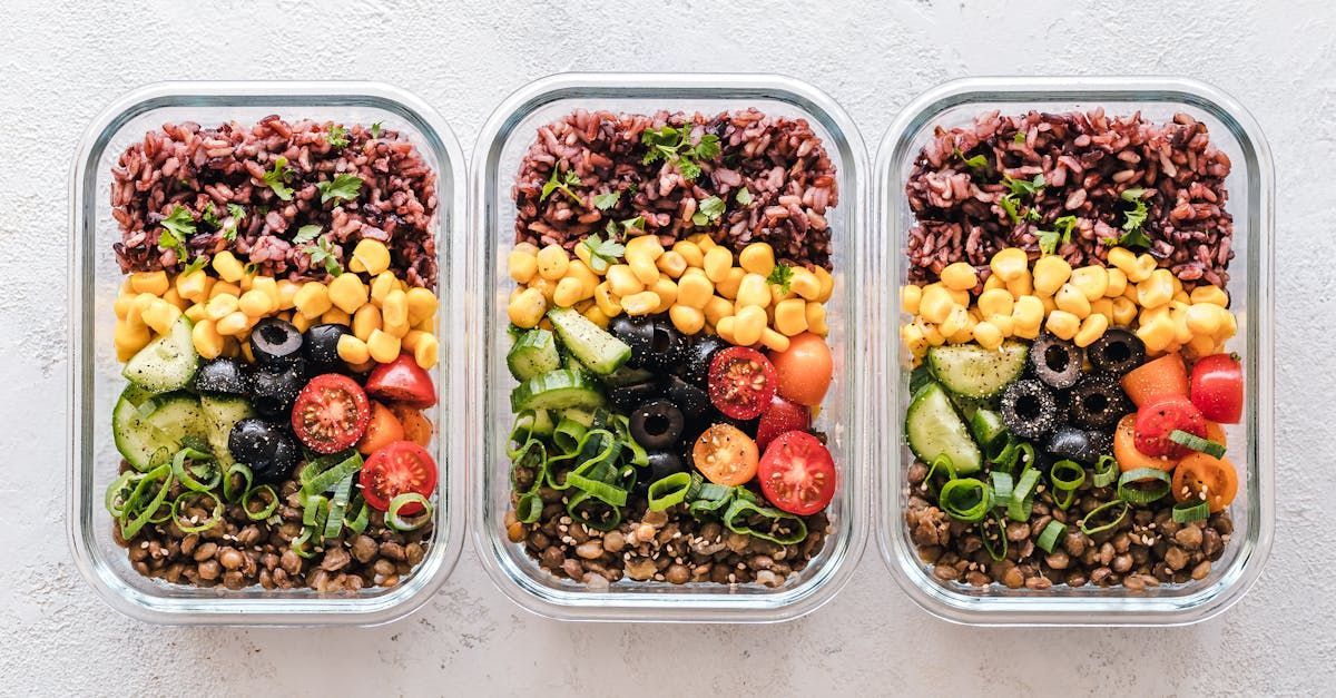 Three meal prep containers with layers of lentils, veggies, corn, olives, and rice.