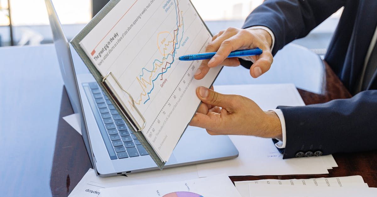 Person in a suit points to a graph on a clipboard over a laptop.